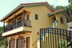 Yellow stucco home with a wrought iron balcony railing and stained wood garage doors