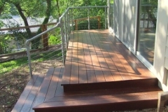 Stained wood deck and steps with a cable railing beside a home